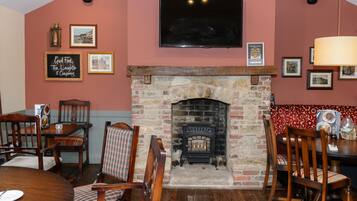 A cozy dining area with a stone fireplace, wooden chairs, and a television mounted on the wall.