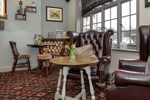 A room with a leather sofa, a wooden chair, a small round table, and a patterned carpet. - Balfour Arms (Sidmouth)