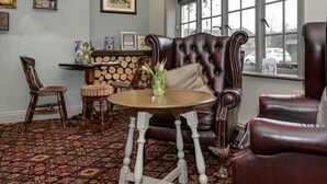 A cozy room with a leather sofa, a wooden chair, a small round table, and a patterned carpet. - Balfour Arms (Sidmouth)