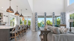A spacious kitchen with a central island, dining area with wicker chairs, and a view of the outdoors. - Amie House BEACH Getaway *GOLF CART ONSITE* (Anna Maria)