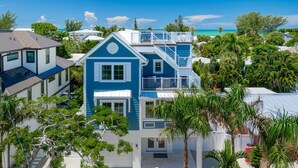 A coastal residential area with a prominent blue house featuring a balcony and a staircase leading to an upper level. - Amie House BEACH Getaway *GOLF CART ONSITE* (Anna Maria)