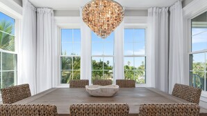 A dining area with a large wooden table, woven chairs, and a central decorative bowl. - Amie House BEACH Getaway *GOLF CART ONSITE* (Anna Maria)