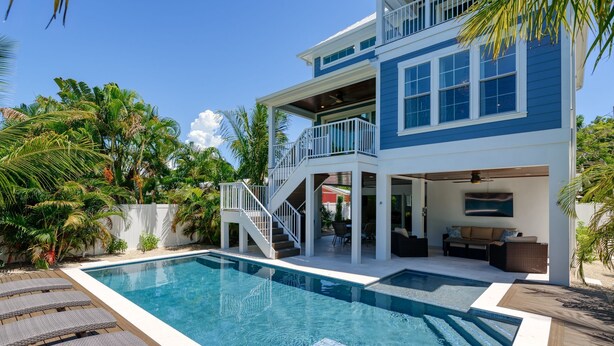 A two-story house with a swimming pool, outdoor seating, and a staircase leading to a balcony. - Amie House BEACH Getaway *GOLF CART ONSITE* (Anna Maria)