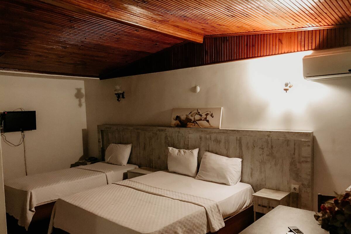Ein Hotelzimmer mit zwei Betten, einer Holzbalkendecke, einem Wand-Fernseher und einem kleinen Tisch mit Fernbedienungen.