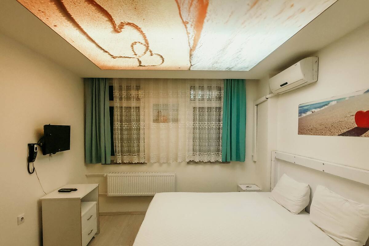 Ein Schlafzimmer mit einem Bett, einem Schreibtisch, einem Telefon, einem Heizkörper und einer Decke mit Herzmuster.