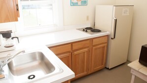 A kitchen with a stainless steel sink, wooden cabinets, a white countertop, a stove, and a refrigerator. - Fountain Point - Cottage 14 (Lake Leelanau)