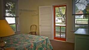 A bedroom with a bed, a chair, a lamp, a door, and a window. - Fountain Point - Cottage 14 (Lake Leelanau)