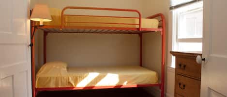 A bunk bed room with a window, a lamp, and a wooden dresser.