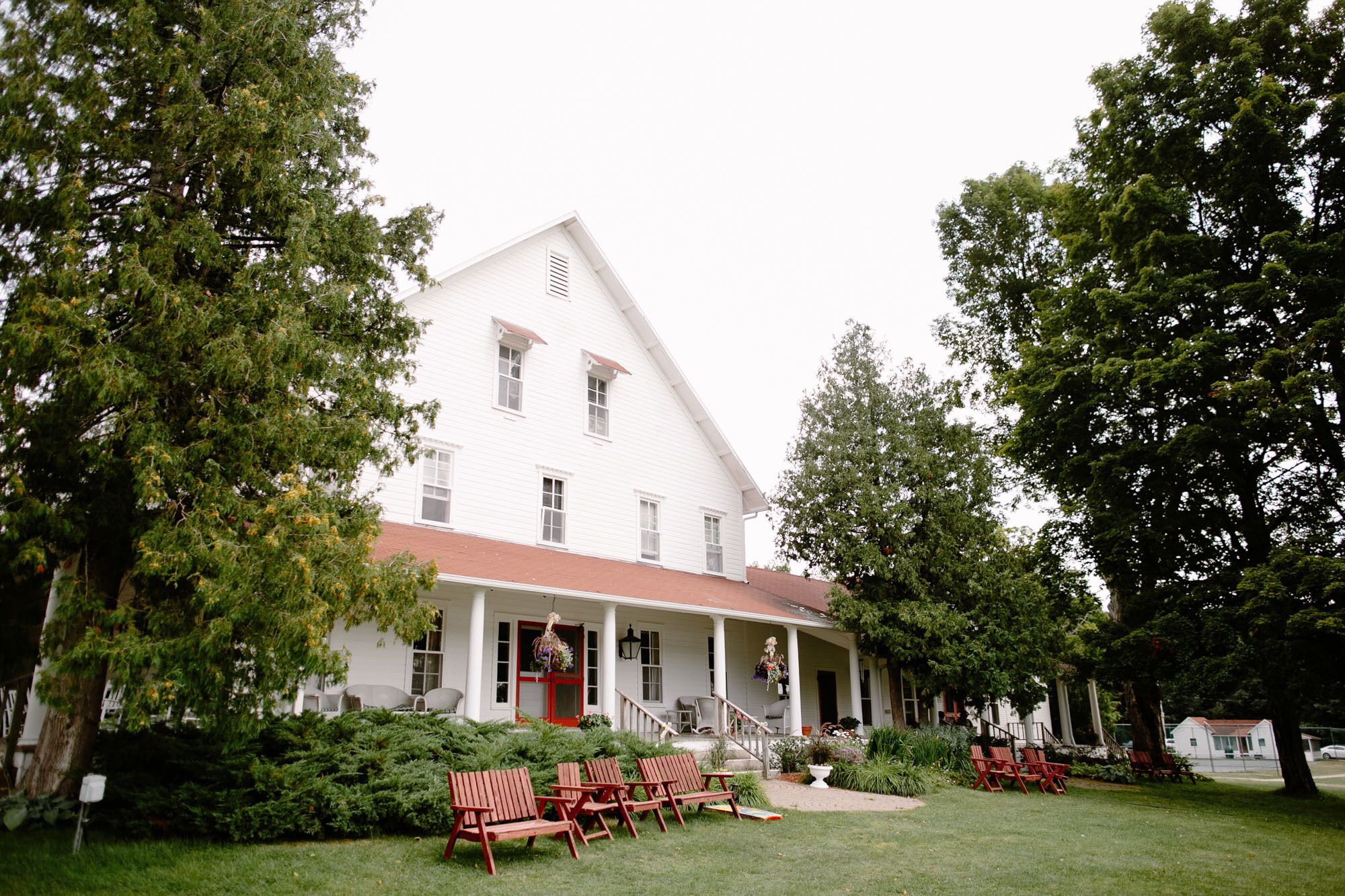 A large white building with a red roof, surrounded by lush greenery and outdoor seating.
