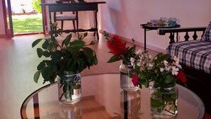 A living room with a glass table holding three vases with plants, a sofa, and a coffee table with cups.