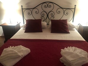 A bed with a red blanket and two pillows, a white bedspread, and two white towels folded on the bed.