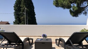 A terrace with two lounge chairs and a small table, overlooking a clear view of the sea.