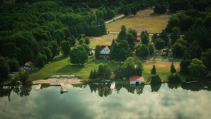 An aerial view of a lakeside property with a dock, a small house with a red roof, and a grassy area.
