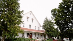 A large white building with a red roof, surrounded by lush greenery and outdoor seating. - Fountain Point - Gebhardt Cottage (Lake Leelanau)