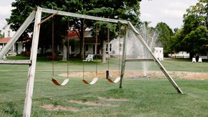 A wooden swing set in a grassy park area with a fountain in the background. - Fountain Point - Gebhardt Cottage (Lake Leelanau)