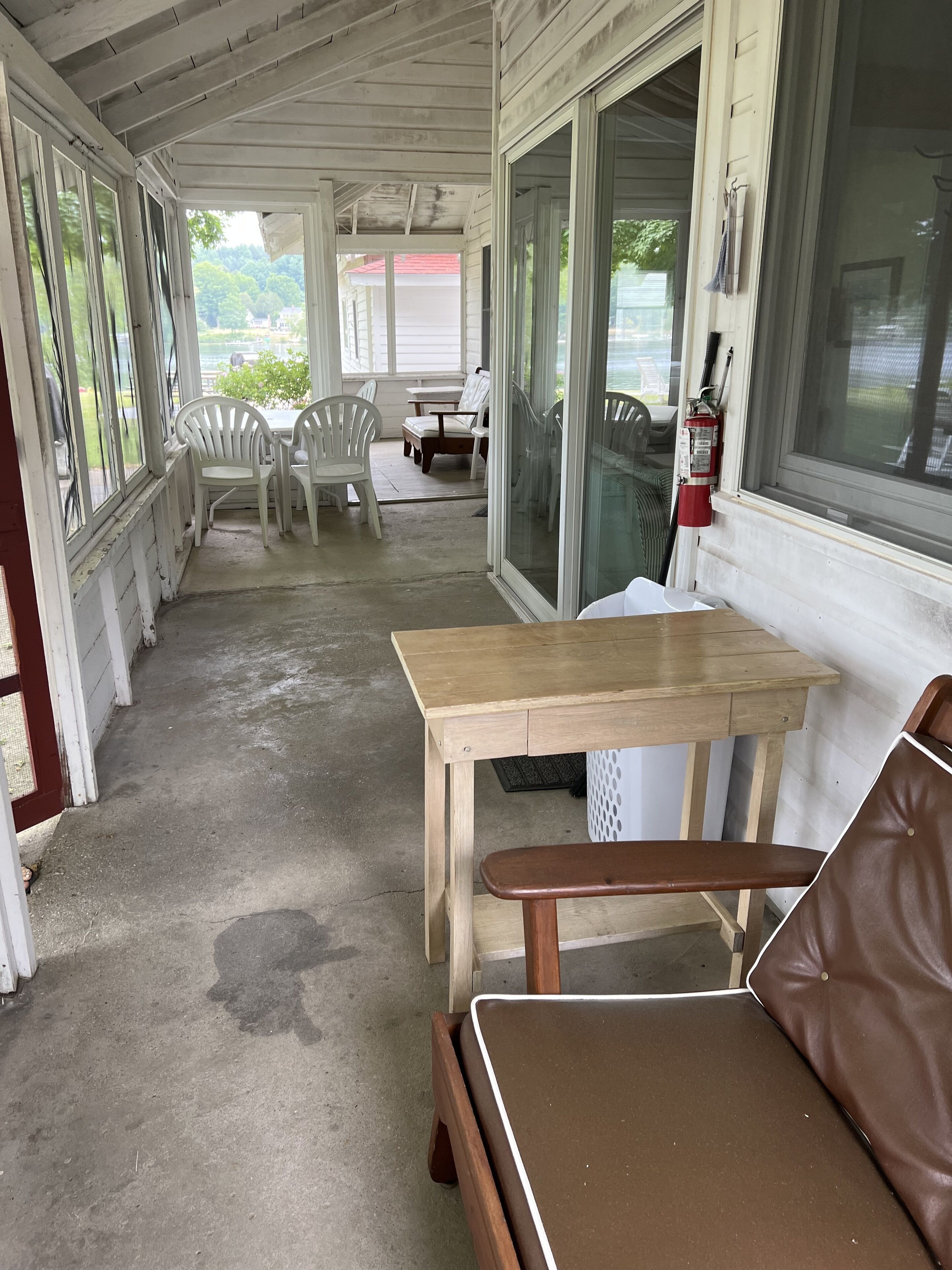 A covered porch with a wooden table and chairs, a fire extinguisher, and a view of the outdoors.