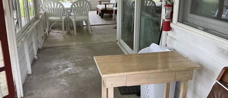 A covered porch with a wooden table and chairs, a fire extinguisher, and a view of the outdoors.