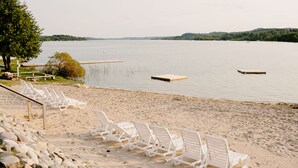 A beach with white lounge chairs and a wooden dock extending into calm water. - Fountain Point - Gebhardt Cottage (Lake Leelanau)