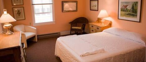A bedroom with a bed, two chairs, a desk, and a window.