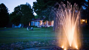 Een fontein met waterstralen in een park, met een huis op de achtergrond.