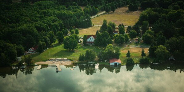 An aerial view of a lakeside property with a dock, a small house with a red roof, and a grassy area. - Fountain Point - Cottage 5 (Lake Leelanau)