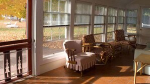 A sunroom with large windows, a wooden table, and several chairs. - Fountain Point - Shepherd Cottage (Lake Leelanau)