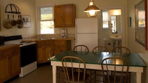 A kitchen with wooden cabinets, a refrigerator, a stove, a dining table with chairs, and a hanging light fixture. - Fountain Point - Shepherd Cottage (Lake Leelanau)