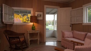 Una habitación acogedora con una mecedora, una mesita con una lámpara, un sofá a rayas y vistas por una puerta abierta.