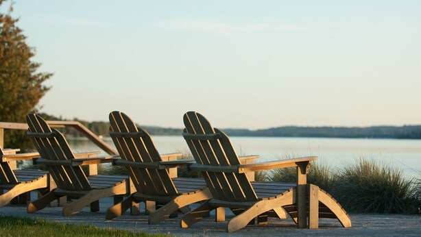 Tres sillas Adirondack de madera con estructura metálica, dispuestas en una terraza junto a un lago tranquilo.