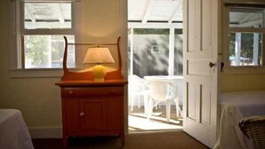 A room with a wooden cabinet, a lamp, a white chair, and a bed. - Fountain Point - Cottage 19 (Lake Leelanau)