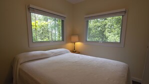 A bedroom with a bed, two windows with blinds, and a bedside lamp.