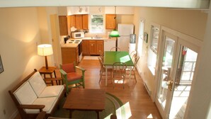 A compact kitchen with wooden cabinets, a microwave, and a sink. There is a dining area with a green table and chairs, and a sofa.