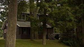 A rustic cabin with a sloped roof, surrounded by dense trees and a well-maintained lawn.