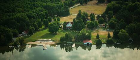 An aerial view of a lakeside property with a dock, a small house with a red roof, and a grassy area.