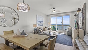 Un vaste espace de vie comprenant une table à manger en bois, un canapé et un balcon offrant une vue sur la mer.
