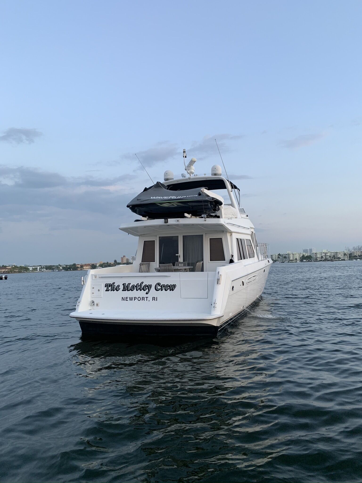 Un yate blanco llamado 'The Motley Crew' con camarote y asientos en la cubierta, amarrado en aguas tranquilas.