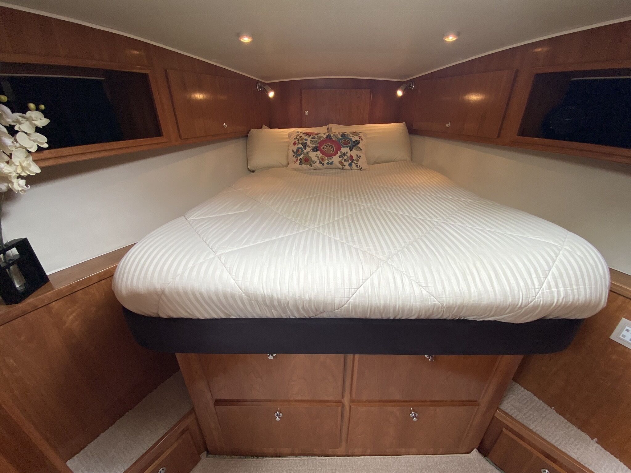 A compact, well-lit cabin with a bed centered under wooden cabinetry, a small bedside table, and a decorative pillow.