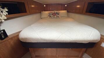 A compact, well-lit cabin with a bed centered under wooden cabinetry, a small bedside table, and a decorative pillow.