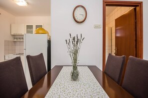 A dining area with a table set for four, featuring a floral tablecloth and a vase with dried flowers.