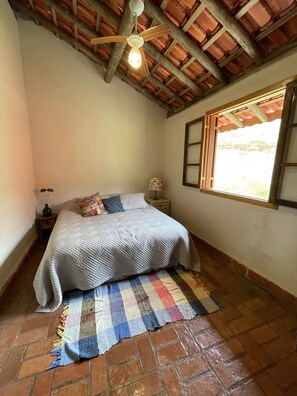 Quarto com cama, teto de madeira, janela e chão de tijolos.
