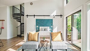 Une chambre à coucher moderne avec un lit, deux fauteuils, une petite table et un escalier.