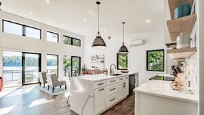 Une cuisine moderne dotée d’un grand îlot central, de luminaires suspendus et de grandes fenêtres offrant une vue panoramique.