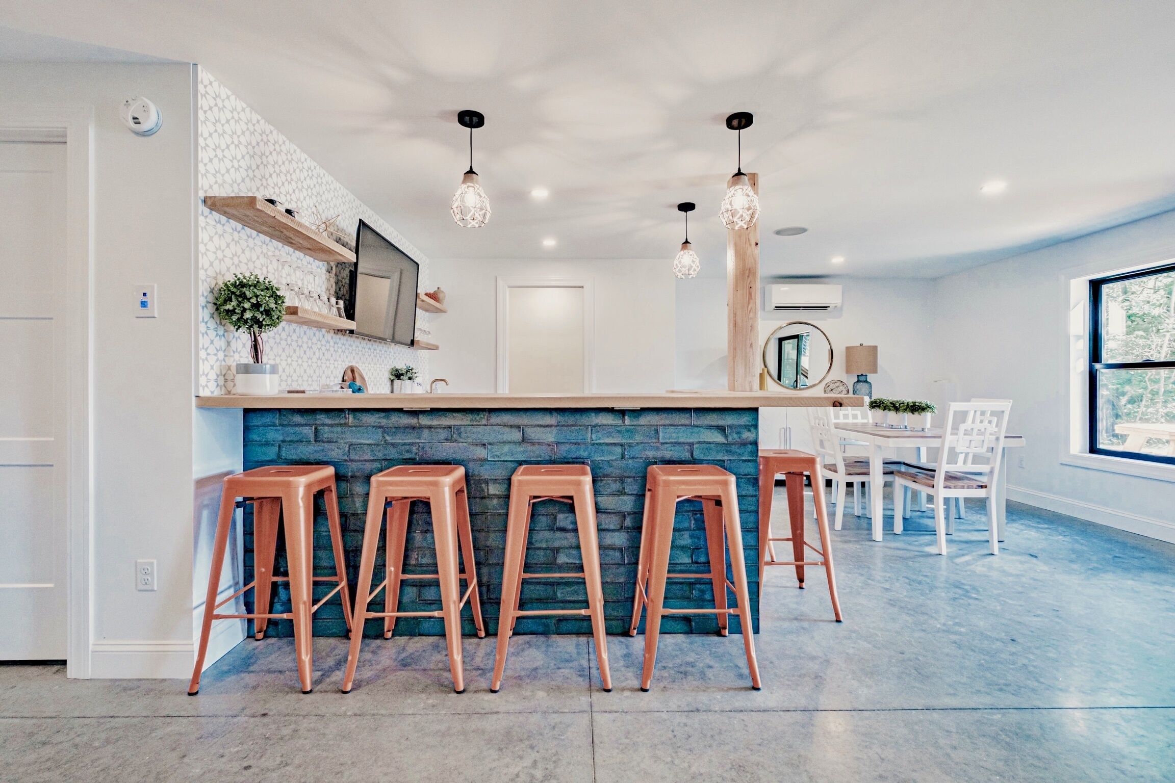 Une cuisine moderne dotée d’un îlot central, de tabourets de bar, de luminaires suspendus et d’un coin repas avec des chaises et une table.