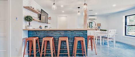 Une cuisine moderne dotée d’un îlot central, de tabourets de bar, de luminaires suspendus et d’un coin repas avec des chaises et une table.
