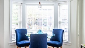 A corner room with a bay window, two blue chairs, a glass table, and a hanging light fixture. - Contemporary  Elegance Meets Coastal decor (Kennebunk)