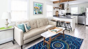 A modern living room with a beige sofa, a coffee table, and a kitchen area with a bar. - Contemporary  Elegance Meets Coastal decor (Kennebunk)