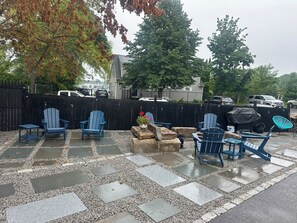 An outdoor seating area with Adirondack chairs and a small table, surrounded by a black fence and trees.