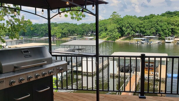 Una terraza con una parrilla, con vista a un lago con muelles y barcos.