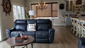 Una sala de estar acogedora con un sofá de cuero negro, una mesa redonda y vistas al área de cocina y comedor.