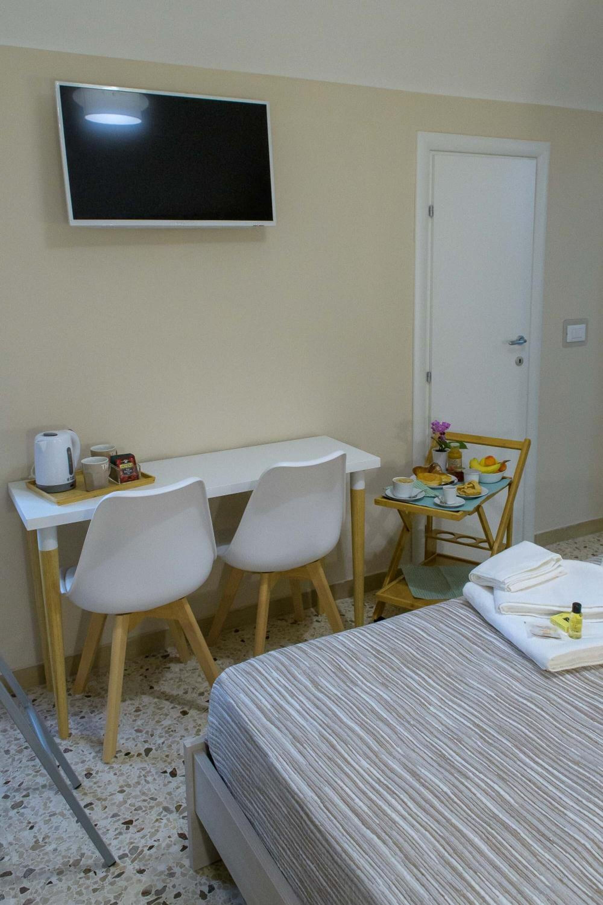 A hotel room with a bed, a desk with two chairs, a television, and a small table with breakfast items.